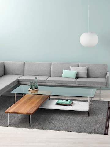 A light gray sectional borders an L-shaped Layer coffee table with three intersecting shelves of glass, wood, and marble.