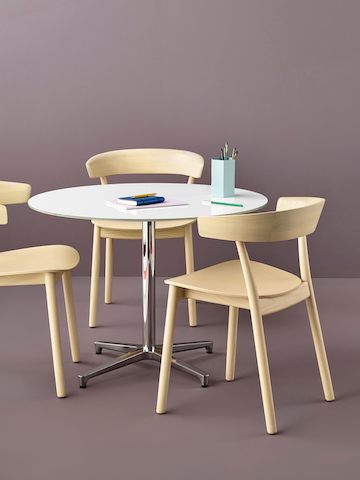 A round Saiba occasional table with a white top surrounded by three all-wood Leeway side chairs with a light finish.