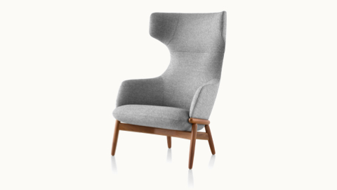Angled view of a wing-back Reframe lounge chair with light gray upholstery and a wood frame with a medium finish.