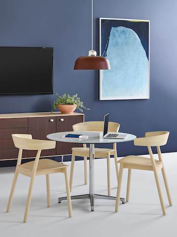 Three Leeway side chairs with a light wood finish complement a round Saiba occasional table with a white top and aluminum pedestal base.
