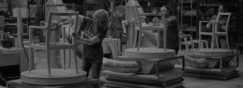 Black-and-white image of Geiger employees assembling side chairs in a manufacturing plant.