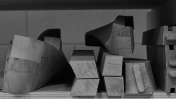 Black-and-white image of various unfinished wood furniture pieces stacked together.