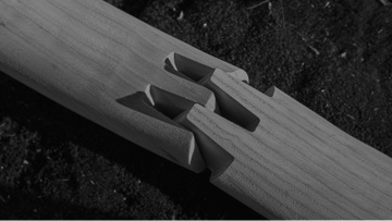 Black-and-white image of a dovetail joint, slightly separated, between two pieces of wood.