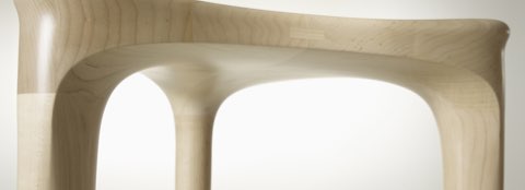Partial view of the seat of a 2 by 3 Stool with a light wood finish.