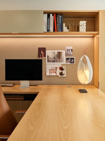 Geiger One Casegoods in Natural Flat Cut Oak with a Geiger Taper Chair by Mark Goetz viewed from the side with office accessories including a table lamp and books in overhead storage, in a private office in the Geiger DatesWeiser Chicago Showroom.