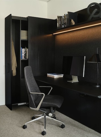 Geiger One Casegoods in Ebonized Flat Cut Ash veneer shown at an angle with an open wardrobe, overhead shelf with integrated lighting, and Taper chair.