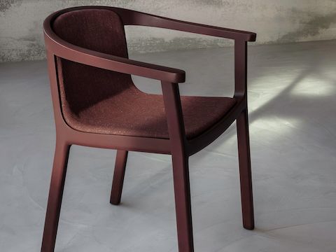 Lijn Chair designed by Carole Baijings for Geiger with upholstered seat and back and tinted wood frame in Red Clay viewed at an angle in a styled environment.