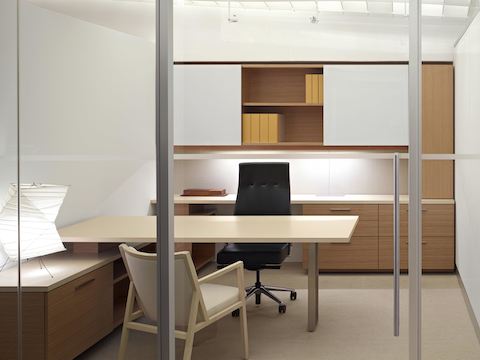 A view into a glass-walled office featuring Geiger Levels Casegoods, a black leather Geiger Sotto Chair, and an ivory-colored Ascribe guest chair.