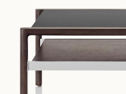Partial view of a Brabo coffee table, showing the mix of materials, including a black leather-wrapped top, walnut lower shelf, and metal frame supports.