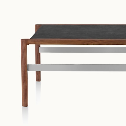 Partial front view of a rectangular Brabo coffee table with a black leather-wrapped top, walnut frame, and steel-plated metal frame supports.