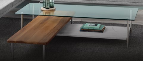 An L-shaped Layer coffee table with a glass top, stone lower shelf, and perpendicular wood shelf.