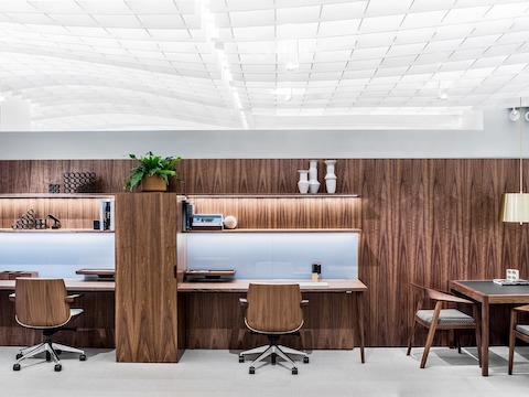 Two adjacent workstations featuring Clamshell office chairs with veneer shells that coordinate with the wood finish on the wall, surfaces, and storage.