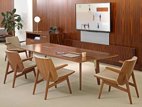 An open meeting area featuring a large wall-hung monitor, rectangular Geiger Elsi conference table, and four low-back Clamshell Lounge Chairs.