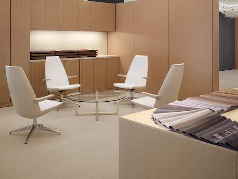 A meeting space featuring a round Loophole coffee table with a glass top surrounded by four off-white Clamshell Lounge Chairs with high backs.