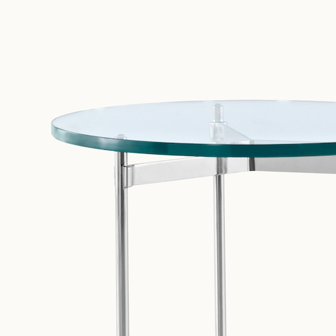 Partial view of a round Claw occasional table, showing the metal cross brace that grasps the tubular legs beneath the glass top.