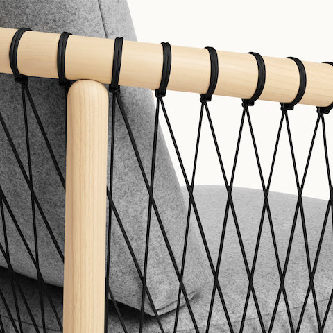 Close-up on the side of a Crosshatch lounge chair, showing the black parachute cords that form a lattice to support the wood frame.