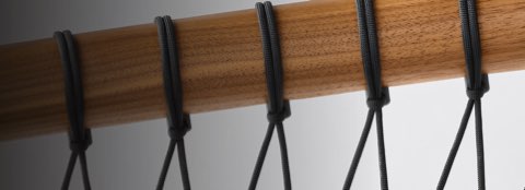 A detailed shot of the black parachute cords wrapping around the walnut frame of the Crosshatch Settee.
