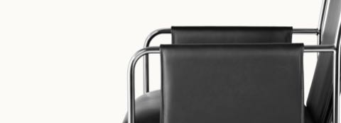 Partial side view of an Envelope side chair, showing how the black leather upholstery wraps around the tubular steel arms.