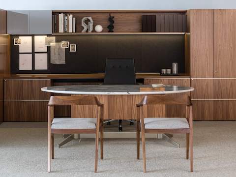 An executive office featuring an oval MP Height-Adjustable Table with a stone top and two Full Twist Guest Chairs with light gray seats.