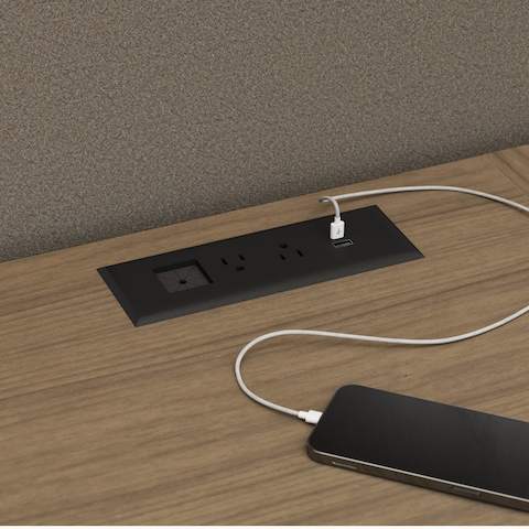 Detail shot of an in-surface power module charging a mobile phone in a Geiger One Private Office in Natural Flat Cut Walnut.