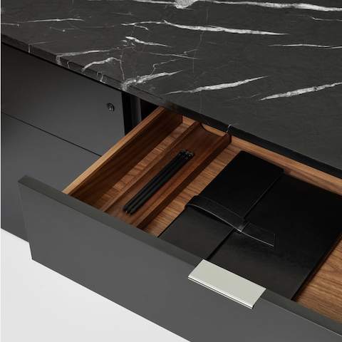 Detail shot of a black Geiger One Casegoods credenza with a Nero Marquina top and an open drawer with a chrome pull tab and walnut interiors.