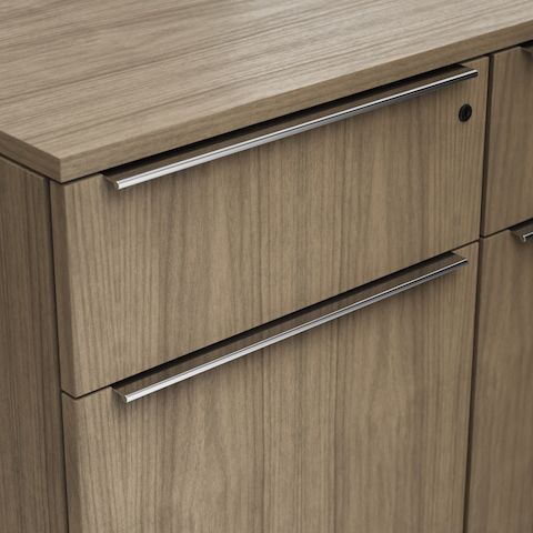 Detail shot of the Geiger One Casegoods full tab pull option in Chrome on a Natural Flat Cut Walnut drawer front viewed from an angle.
