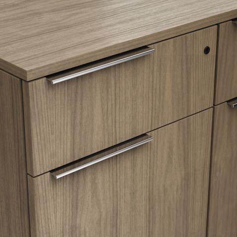 Detail shot of the Geiger One Casegoods offset tab pull (left) option in Chrome on a Natural Flat Cut Walnut drawer front viewed from an angle.