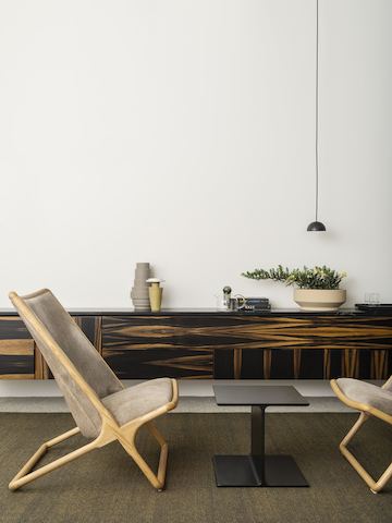 A small interaction space featuring two wood-frame Scissor Chairs on either side of a black I Beam side table.