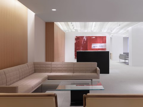 A lobby lounge featuring a beige Tuxedo Component sectional and a square I Beam coffee table with a black pedestal and glass top.