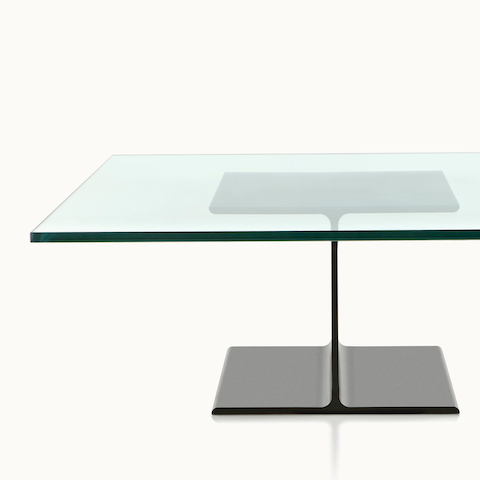 Partial view of a square I Beam coffee table with a glass top and black cast-aluminum pedestal.