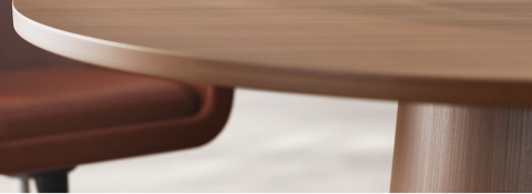 Detail of JD Meeting Table by DatesWeiser showing tapered round base in natural quarter cut walnut with two bumper chairs on a concrete floor. Detail of JD Meeting Table by DatesWeiser showing tapered round base in natural quarter cut walnut with two bumper chairs on a concrete floor.