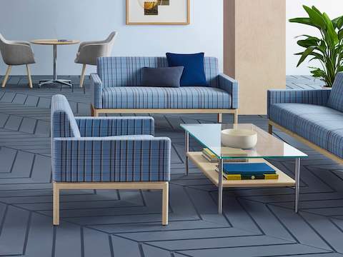 A lounge featuring a rectangular Layer coffee table with a glass top and wood shelf, surrounded by Wood Base Lounge Seating with blue plaid fabric.