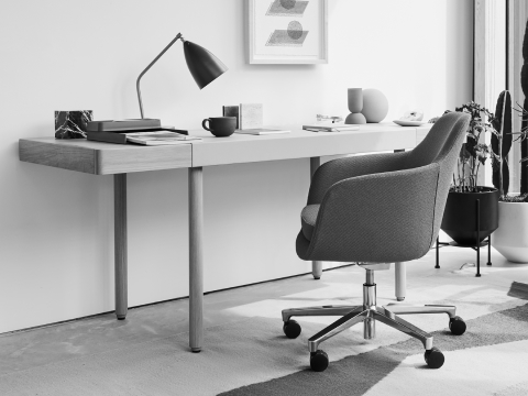 A home office setting with the Leatherwrap Sit-to-Stand Desk, Saiba office chair and Crosshatch Settee.