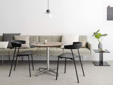 An informal meeting space featuring two black Leeway side chairs, a tan Tuxedo Component sofa, and a round Saiba occasional table.