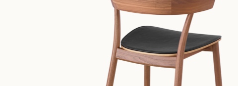 The middle portion of a Leeway side chair, viewed from behind at an angle to show a wood seat with black leather upholstery.