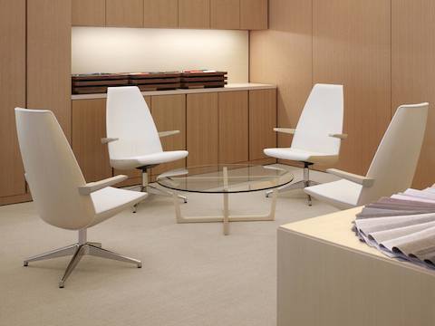 A meeting space featuring a round Loophole coffee table with a glass top surrounded by four off-white Clamshell Lounge Chairs with high backs.