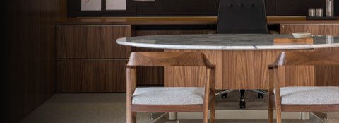 Partial view of an executive office, focusing on an oval MP Height-Adjustable Table with a stone top used as a desk.