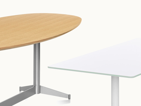 An oblong MP Table with a wood top next to a rectangular MP Table with a white back-painted glass top.