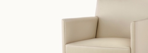 Angled view of the middle portion of a Nessel side chair with wraparound arms and beige leather upholstery.