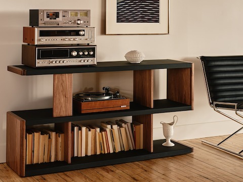 New Canaan Low Bookshelf designed by BassamFellows for Geiger in Walnut with Black Leather shown angled in a residential setting with books and objects on shelves.