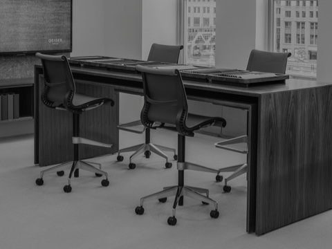 Black-and-white image of a rectangular Peer Table with fabric samples displayed on the surface and a rack of more fabric samples in the foreground.