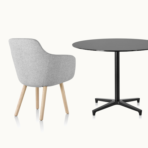 A light gray Saiba Side Chair, viewed from behind at an angle, next to a round Saiba occasional table with a black top and base.