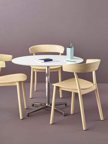 Three Leeway side chairs with a light wood finish complement a round Saiba occasional table with a white top and aluminum pedestal base.