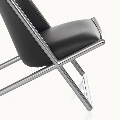 Partial side view of a Scissor lounge chair with black leather upholstery, focusing on the tubular steel frame.