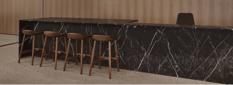 Custom reception desk by DatesWeiser in black stone with four Crosshatch Stools in front of a Natural Oak veneer wall viewed from an angle.