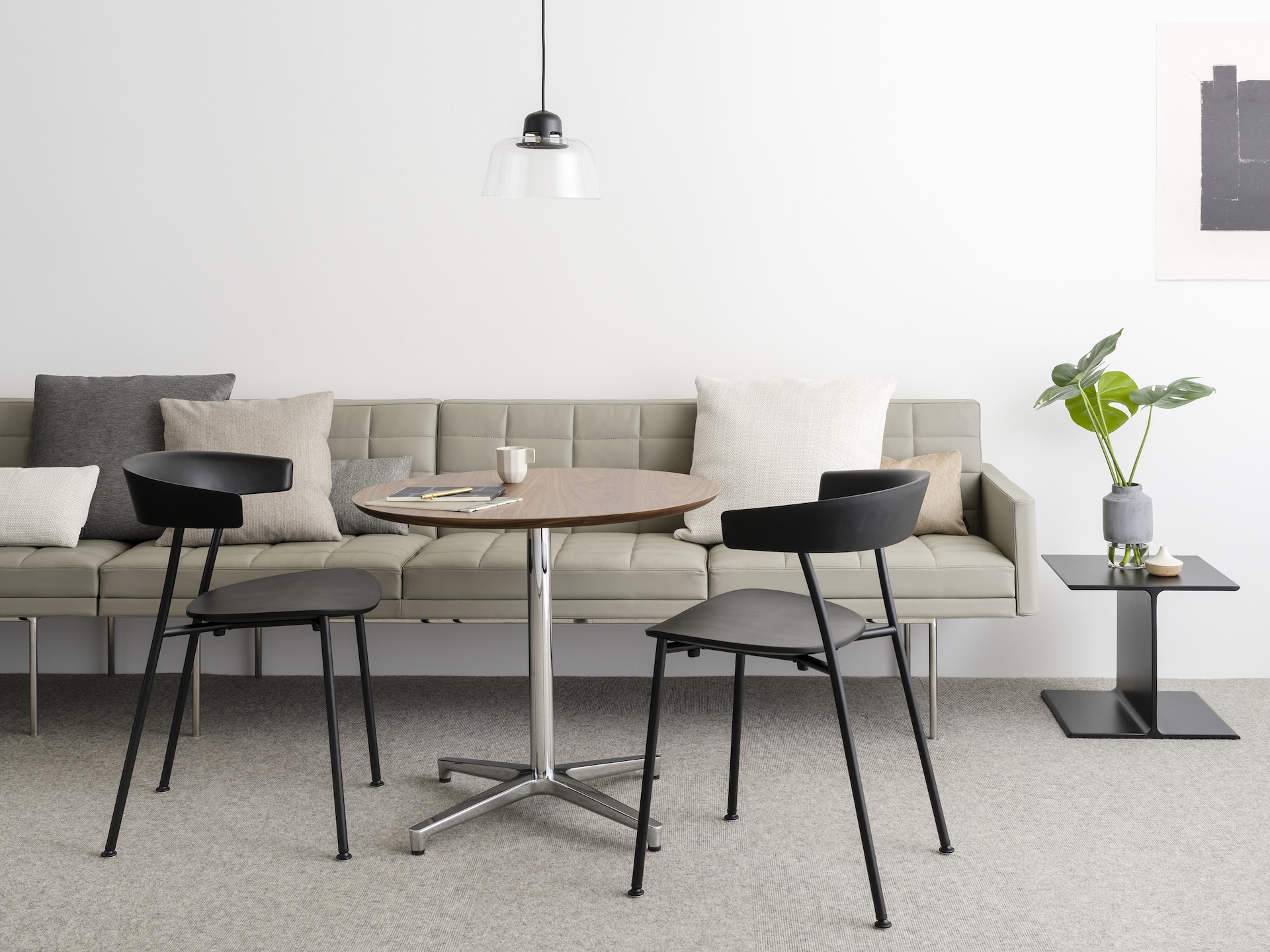An informal meeting space featuring a tan Tuxedo Component sofa, a round Saiba occasional table, and two black Leeway side chairs.